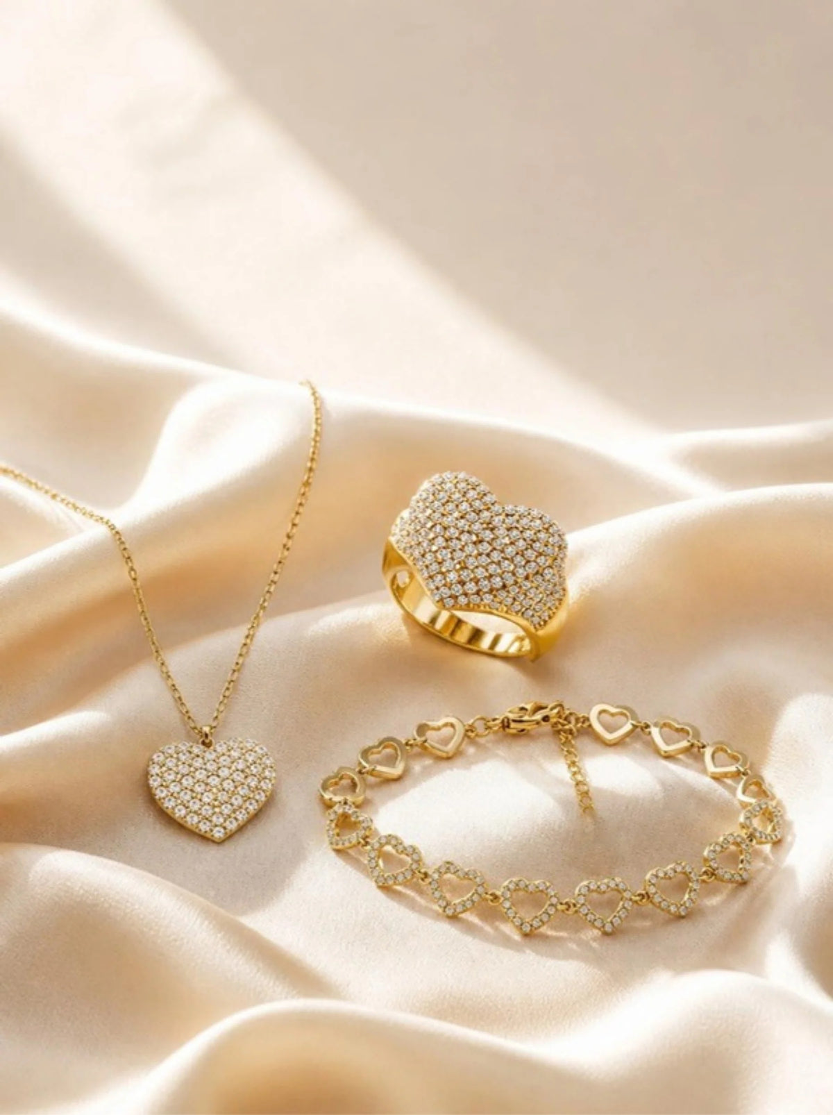 Pavé-Herzkette, Pavé-Herzring und Herzglieder-Armband von AYPARÉ auf cremefarbenem Satin